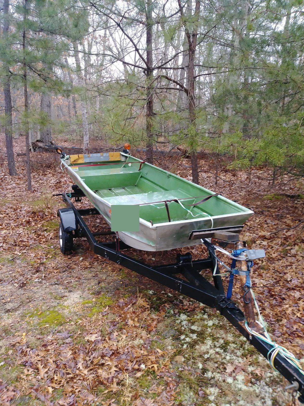 Finished green boat on its trailer among the trees